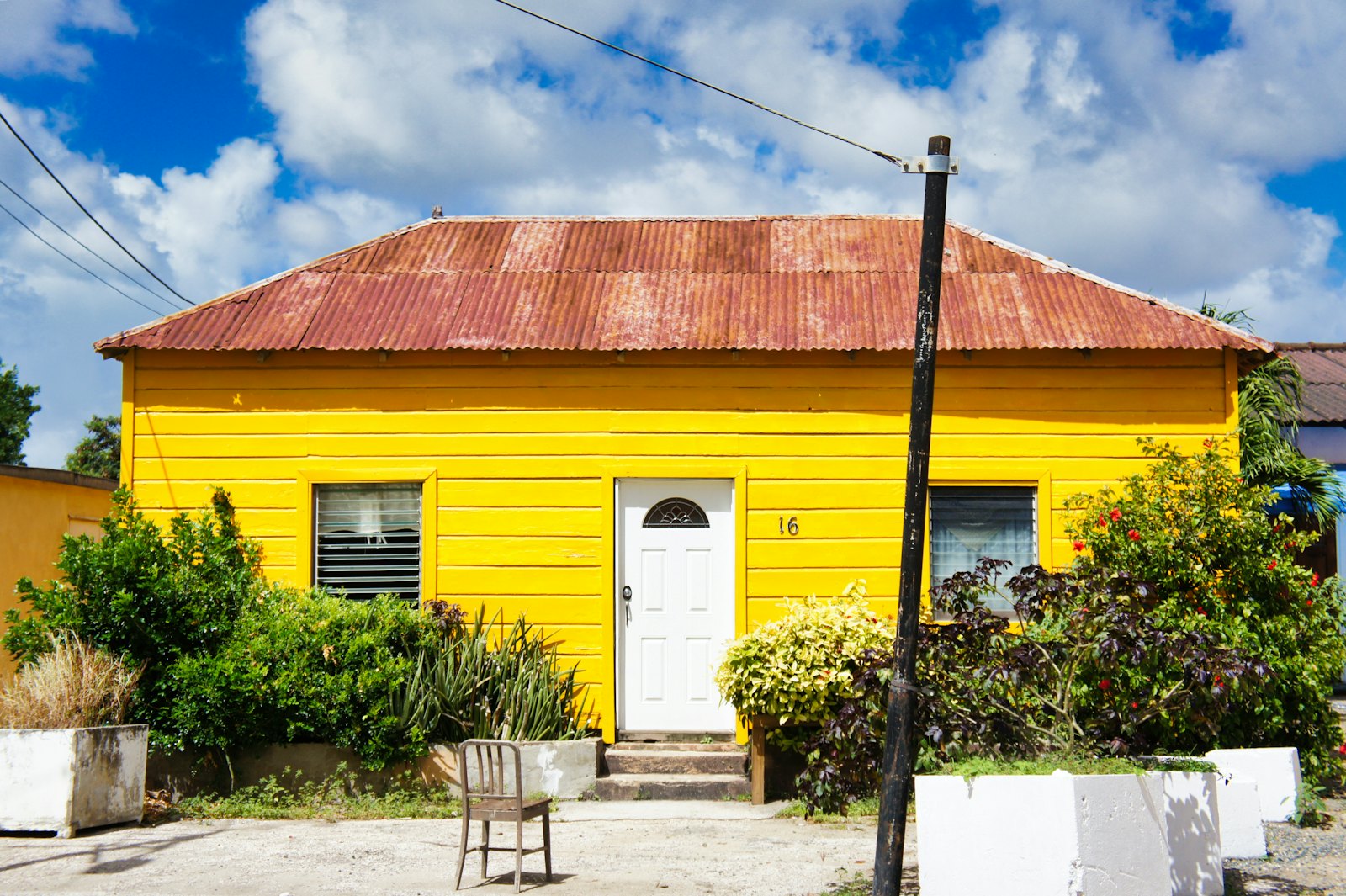 Maison créole aux murs jaunes coiffée d'une toiture en tôle ondulée patinée, sous un ciel des Antilles